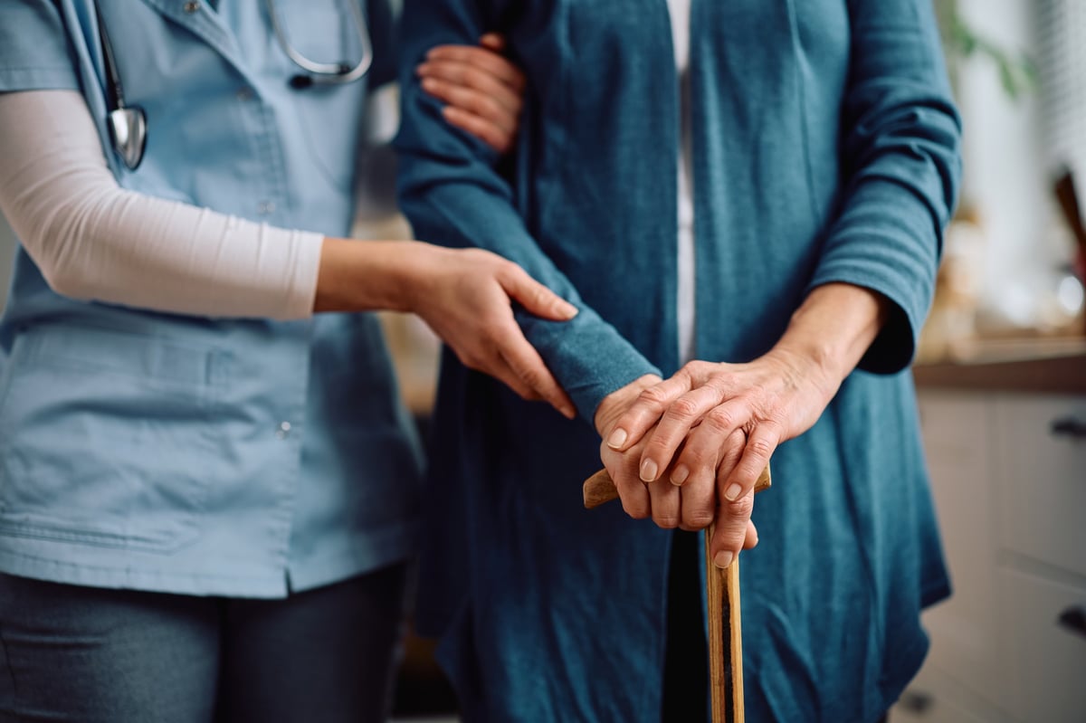 Visiting nurse caring for an elderly woman at home with a walking cane, showing home-based clinical service