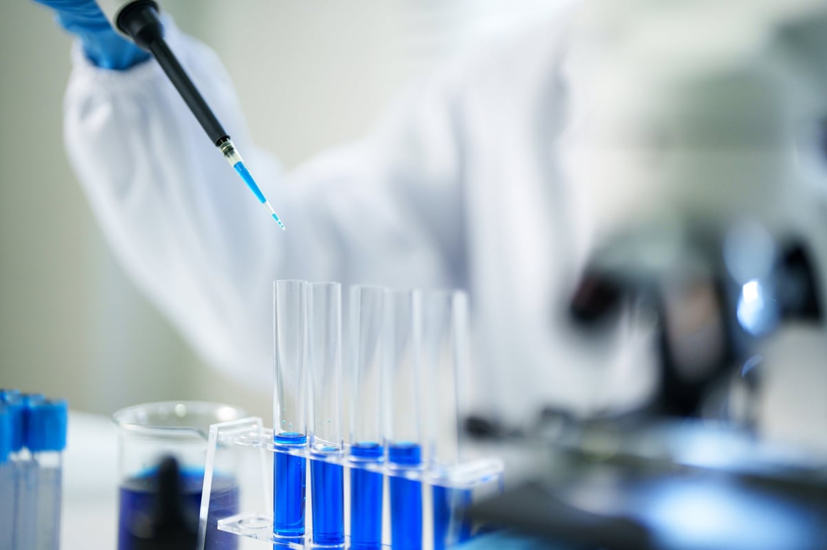 Precise laboratory analysis using a micropipette on blue liquid samples in test tubes