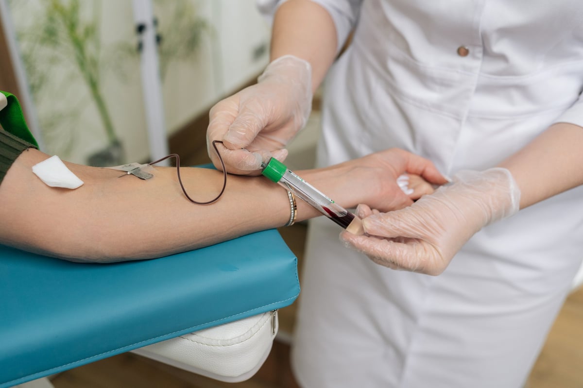 A healthcare professional performing a blood draw on a patient's arm using a vacuum tube system for blood collection